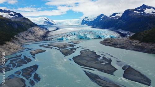 Scenic view of glacial bay with floating ice, waterfalls and towering peaks in the distance.