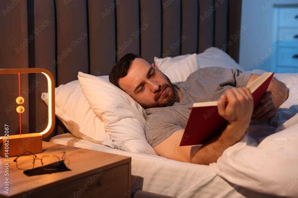 Fototapeta premium Young man reading book in bed at home