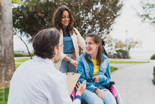 Smiling doctor talking to young woman in wheelchair and caregiver - Happy young woman with cerebral palsy listens to doctor with caregiver beside her - Concept of cerebral palsy 
