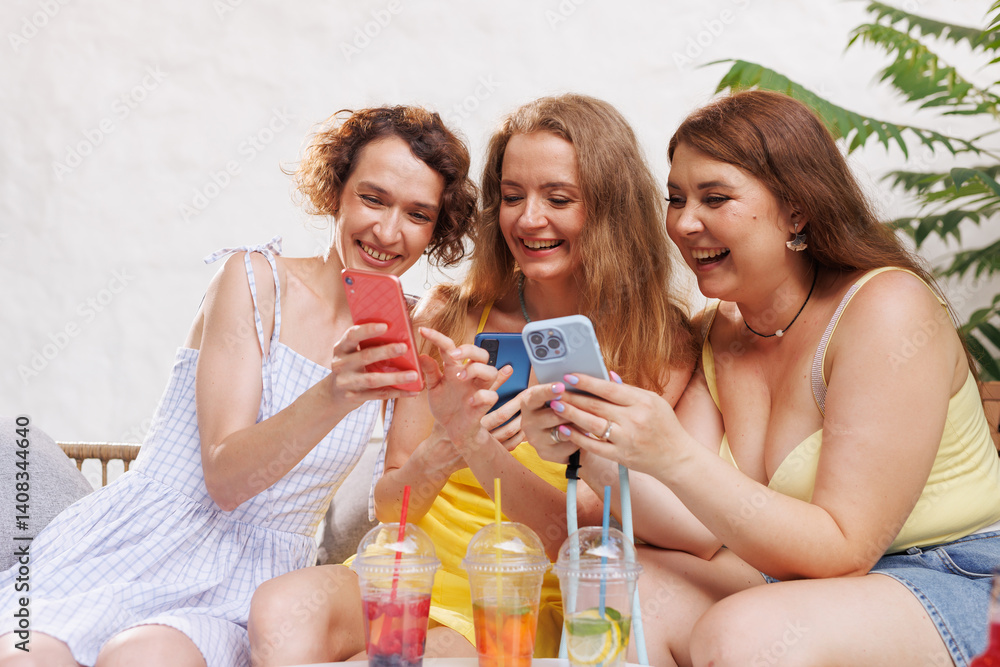 Happy women sharing laughs over smartphones with refreshing drinks in a relaxed summer setting. Happy women sharing laughs over smartphones with refreshing drinks in a relaxed summer setting.