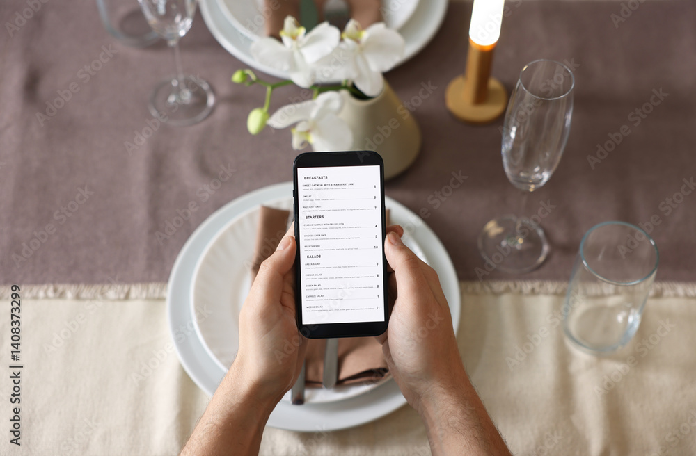 Man choosing dish from digital menu at table in restaurant, top view