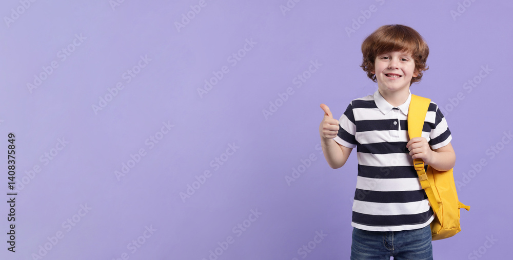 Naklejka premium Cute schoolboy with backpack showing thumbs up on violet background, space for text. Banner