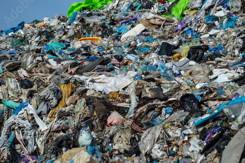 A large accumulation of plastic waste and organic material is visible at a landfill site, highlighting environmental concerns