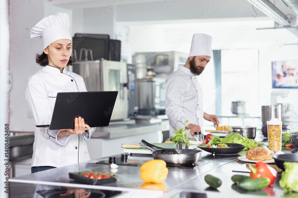 Dedicated chef using a laptop for research while cooking gourmet dishes, in a commercial kitchen balances technology and tradition. Expert chopping vegetables and preparing ingredients. Dedicated chef using a laptop for research while cooking gourmet dishes, in a commercial kitchen balances technology and tradition. Expert chopping vegetables and preparing ingredients.