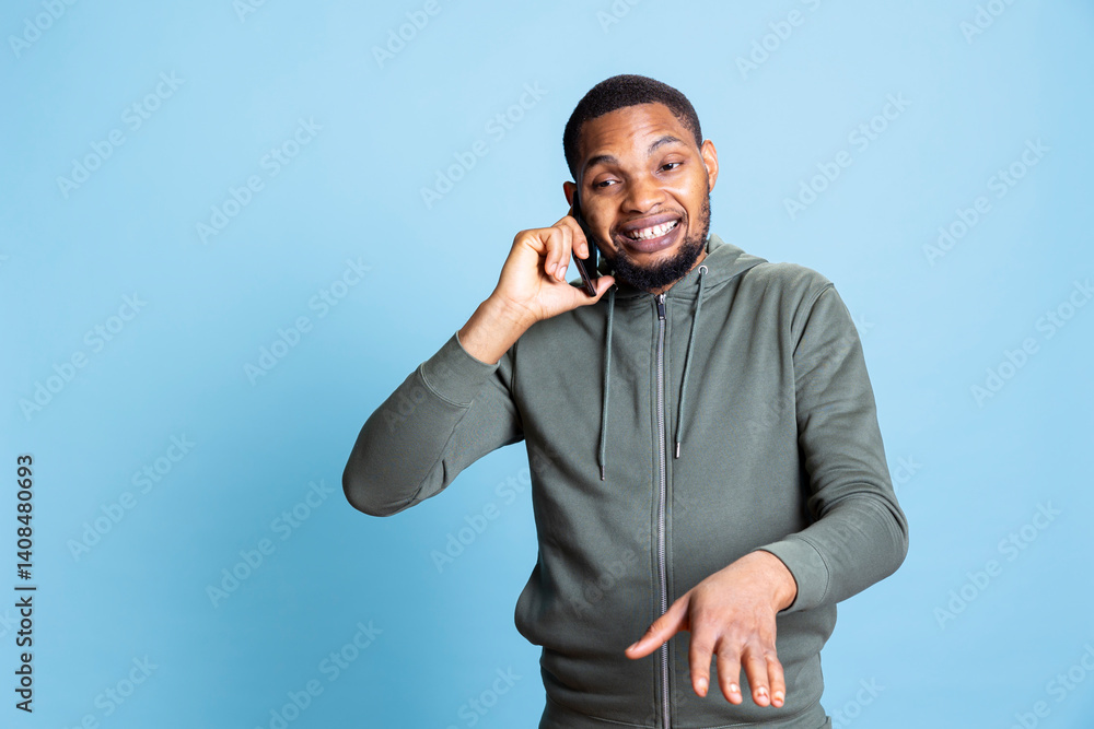 Fototapeta premium African american person chatting on his phone call with friends, gossiping and enjoying his leisure time against blue background. Casual relaxed guy being pleased with his conversation.