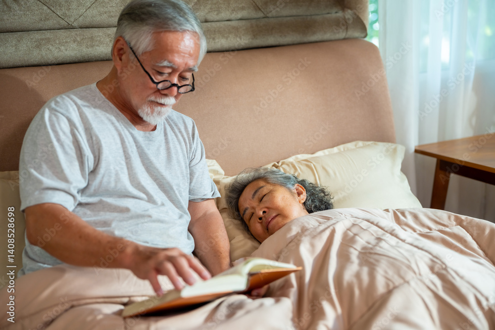 Fototapeta premium Asian senior man reading a book while his wife sleeping on the bed in bedroom. Elderly man suffering with insomnia. Retired people medical healthcare and mental health concept.
