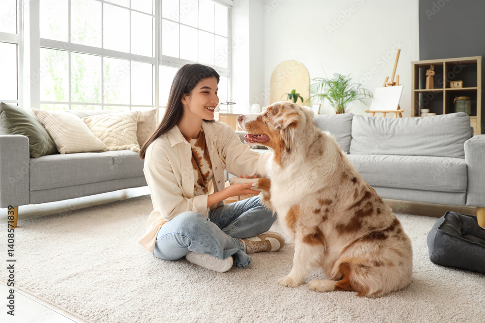 Young woman holding Australian Shepherd dog's paws at home