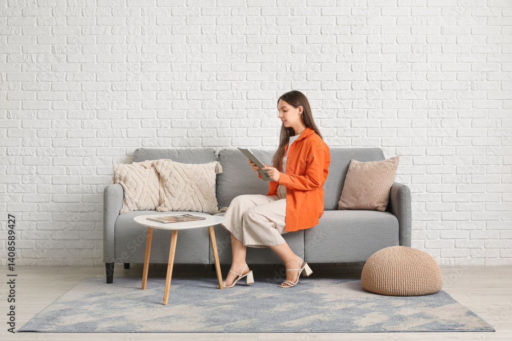 Young pretty woman with magazine resting on grey sofa at home