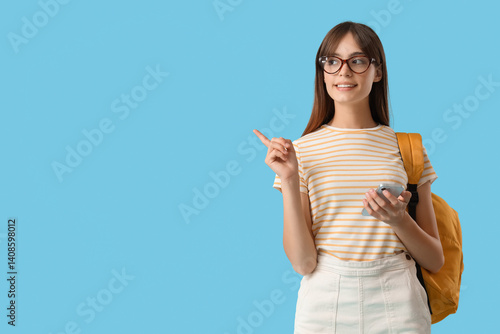Quadro em tela Happy female student with mobile phone and backpack pointing at something on blu