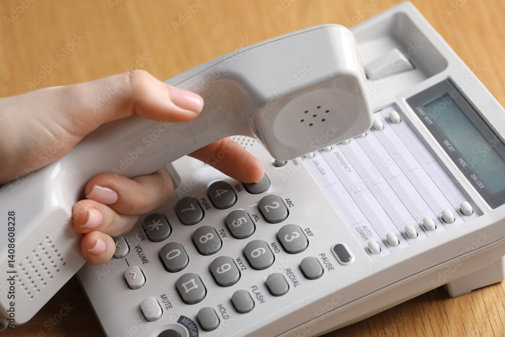 Woman dialing number on telephone at wooden table, closeup Woman dialing number on telephone at wooden table, closeup