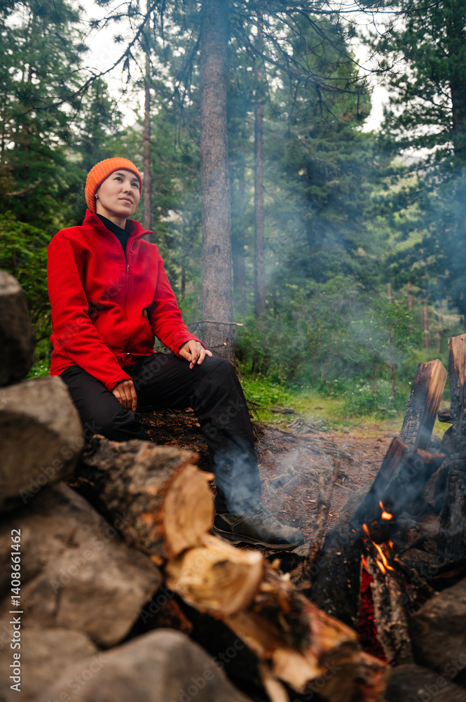 Naklejka premium A girl sits by a campfire in the forest