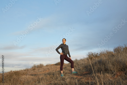 Woman wearing fitness clothes posing after a hike on top of a hill.