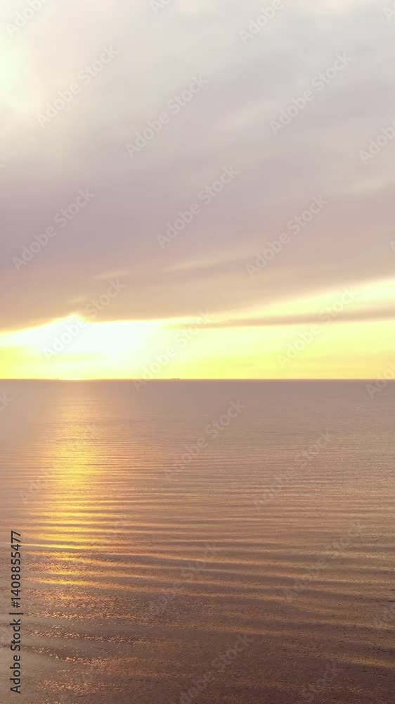 Soft waves reflecting the golden light of the setting sun on the calm Baltic Sea near Garupe Beach, creating a peaceful and serene atmosphere in Latvia, vertical drone shot Soft waves reflecting the golden light of the setting sun on the calm Baltic Sea near Garupe Beach, creating a peaceful and serene atmosphere in Latvia, vertical drone shot
