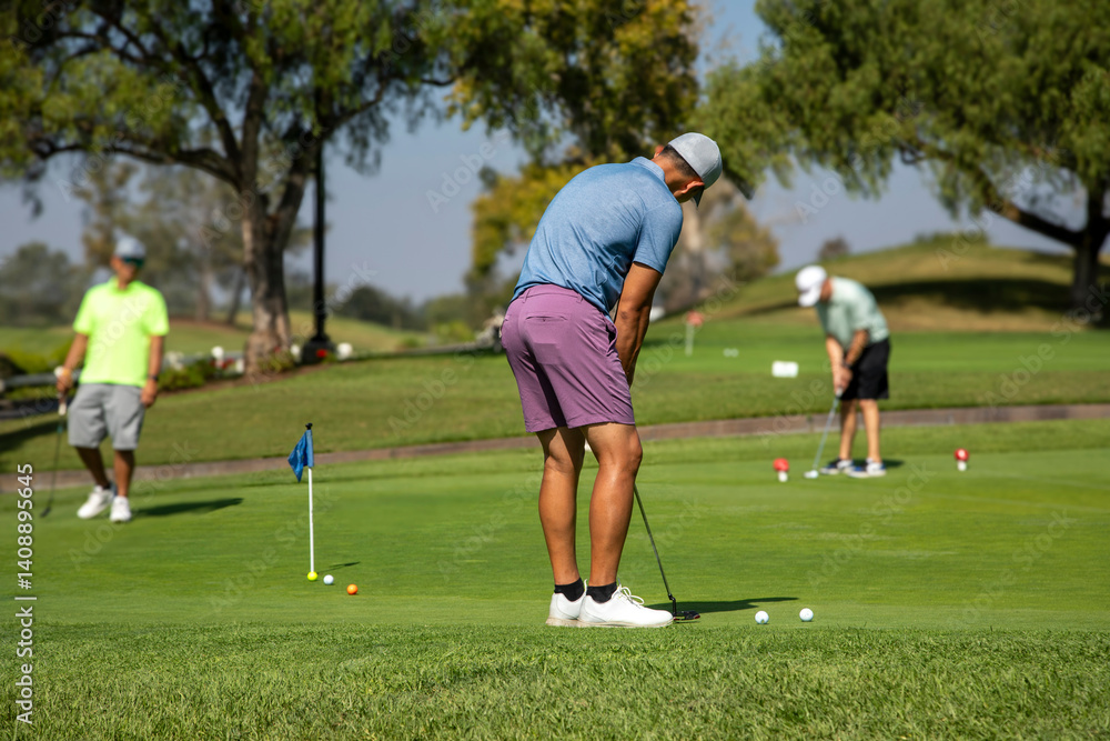 Obraz premium A man wearing a purple shirt putting at a practice green with other golfers in the background