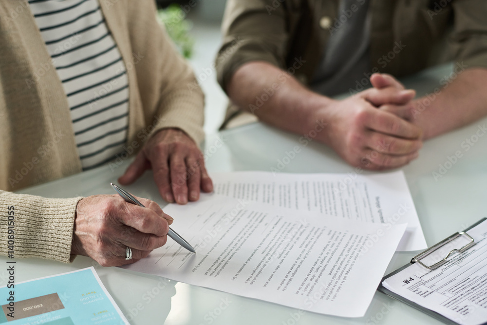 Close-up of senior couple signing documents at table in office