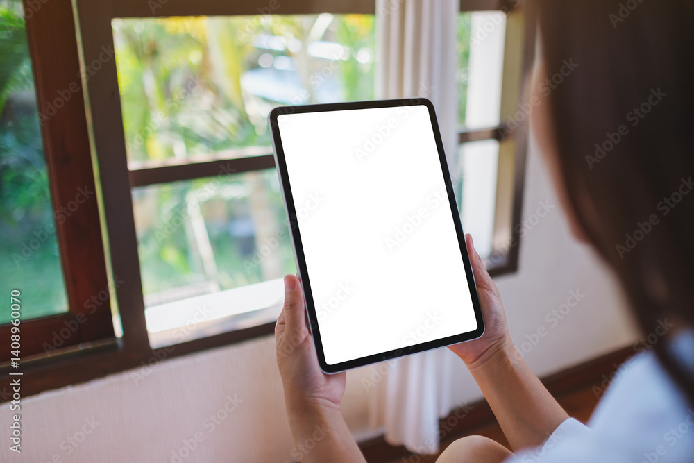 Mockup image of a woman holding tablet with blank desktop white screen on the bed at home