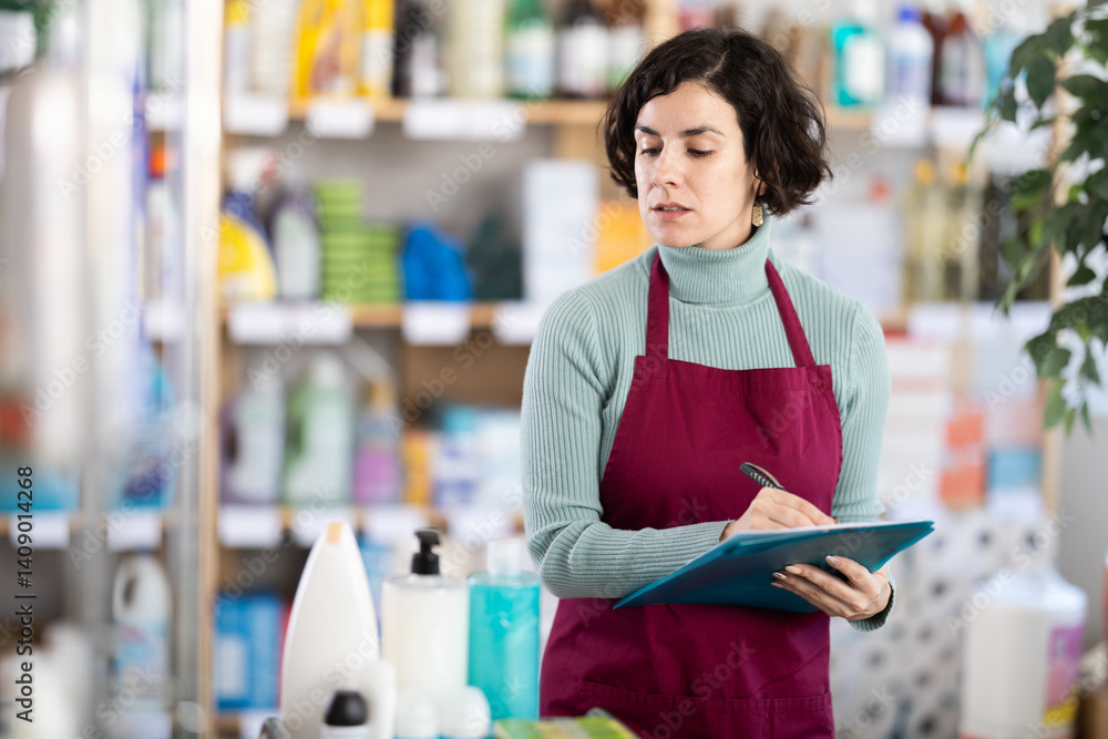 Adult woman seller in uniform conducting inventory in household chemicals store