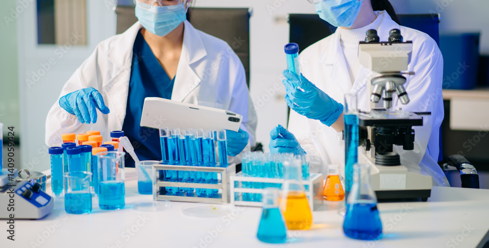 Fototapeta premium Two Asian female biotechnologists in lab coats conduct research, handle glassware, and test chemicals in a modern science lab
