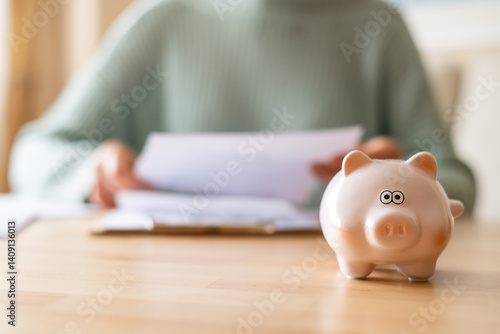 Fototapet Woman reviewing domestic bills while managing monthly expenses, with a piggy ban
