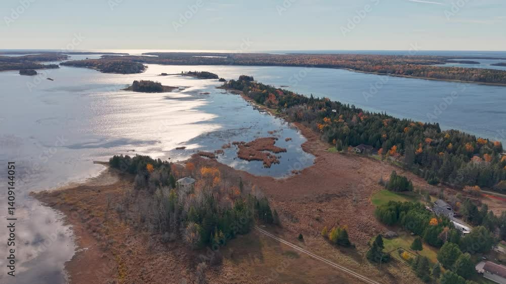 Drone shot of a rugged peninsula jutting into a lake in Michigan’s Upper Peninsula, with autumn trees and sunlit reflections on the water Drone shot of a rugged peninsula jutting into a lake in Michigan’s Upper Peninsula, with autumn trees and sunlit reflections on the water
