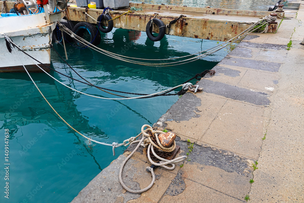 A boat is securely moored at an old pier, with various ropes tied neatly.