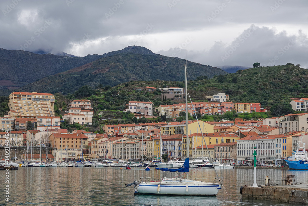 Sailboats float in the calm water of the harbor, surrounded by vibrant buildings. Porte-Vendre, France.