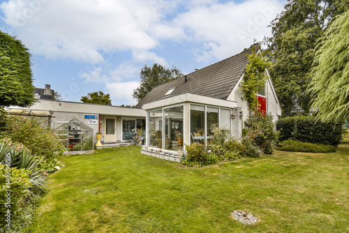 A modern house featuring large glass windows sits amidst a vibrant green garden, showcasing a blend of architecture and nature.