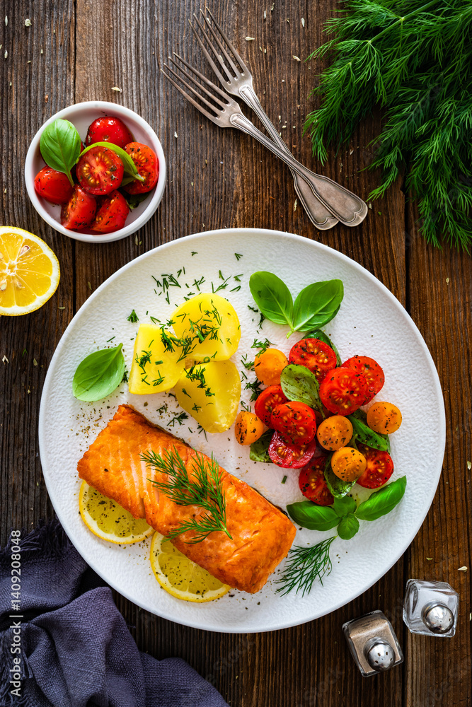 Seared salmon steak with cherry tomatoes and boiled potatoes on wooden table