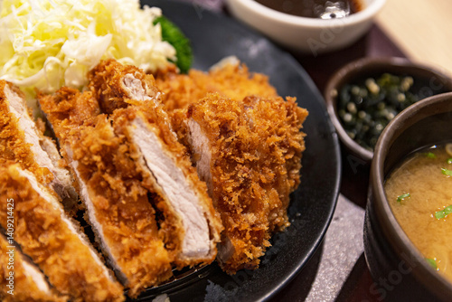 Close-up of Japanese loin katsu with crispy breaded pork loin cutlet, served with shredded cabbage, dipping sauce, and miso soup on a dark plate