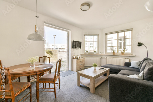 Wallpaper Mural A stylish living area showcases a cozy sofa, a dining table, and large windows allowing natural light to fill the space. The design emphasizes comfort and simplicity. Torontodigital.ca