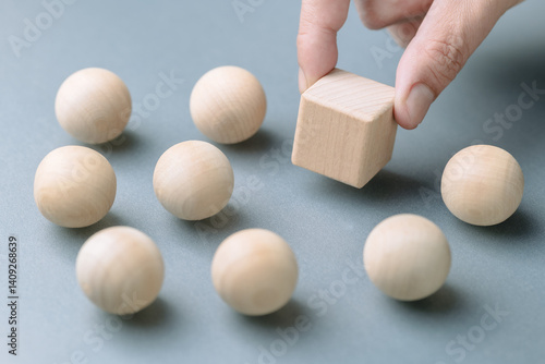 A man's hand is placing a wooden cube among many wooden balls,  concept of positioning in a competitive market, creating a differentiated brand