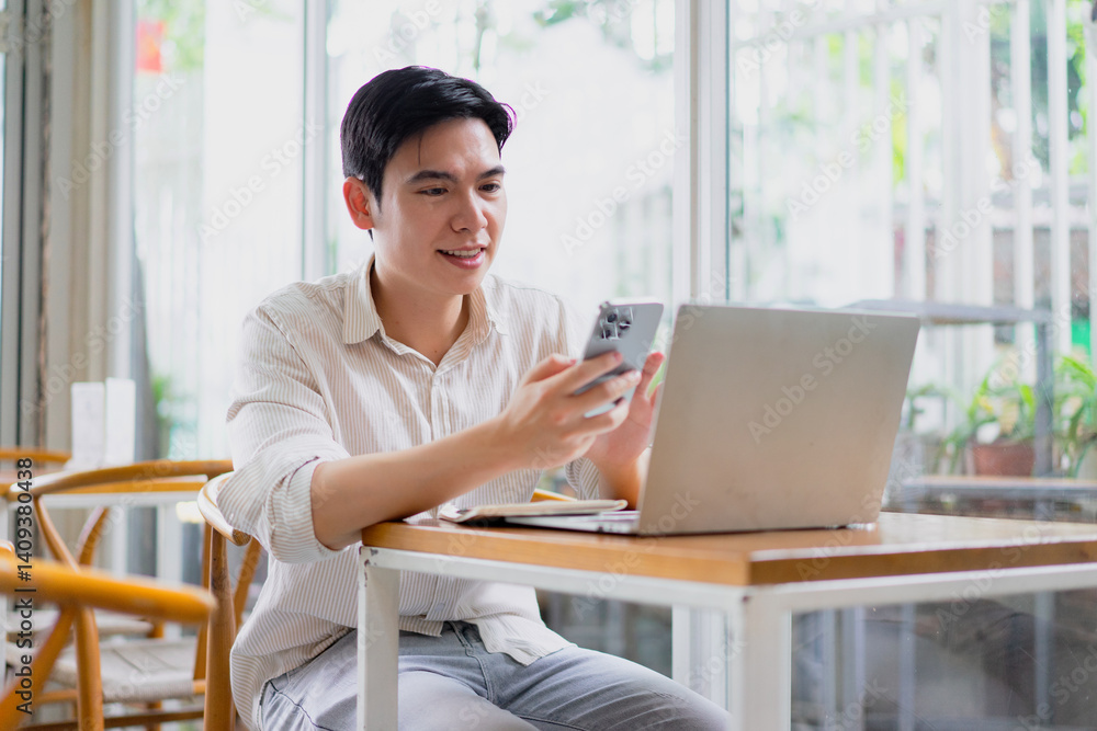 Young man engages with smartphone while working on laptop at a cozy cafe in urban setting during daylight hours Young man engages with smartphone while working on laptop at a cozy cafe in urban setting during daylight hours