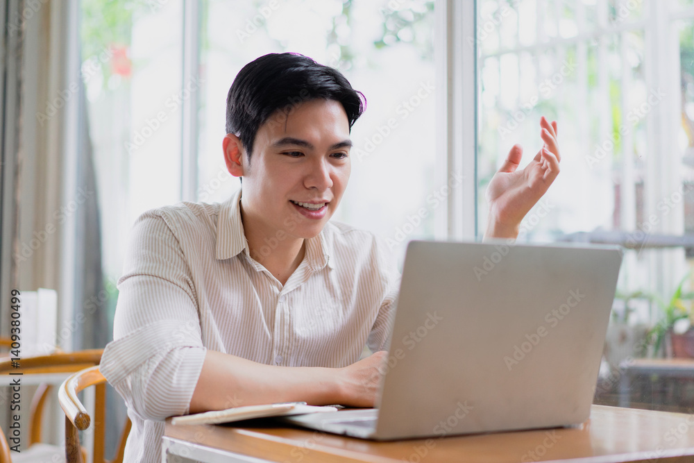 Young Asian man engaged in a lively discussion while working on a laptop at a modern workspace during the afternoon Young Asian man engaged in a lively discussion while working on a laptop at a modern workspace during the afternoon