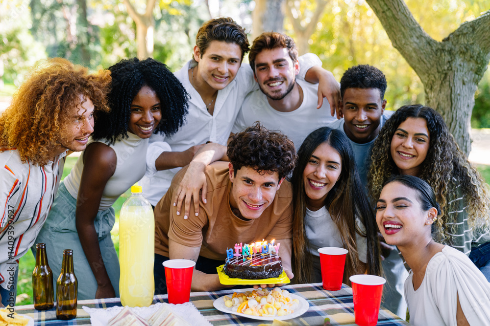 Fototapeta premium Group of cheerful multi ethnic friends celebrating a birthday with cake and drinks at an outdoor party