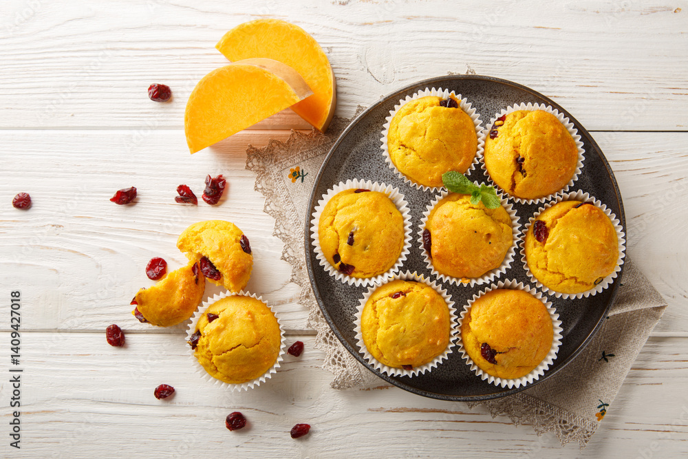 Freshly baked pumpkin muffins with dried cranberries, orange zest and spices close-up in a plate on the table. Horizontal top view from above