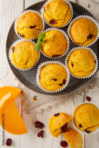 Delicious pumpkin cranberry muffins are made with pumpkin puree and dried cranberries closeup on the plate on the wooden table. Vertical top view from above