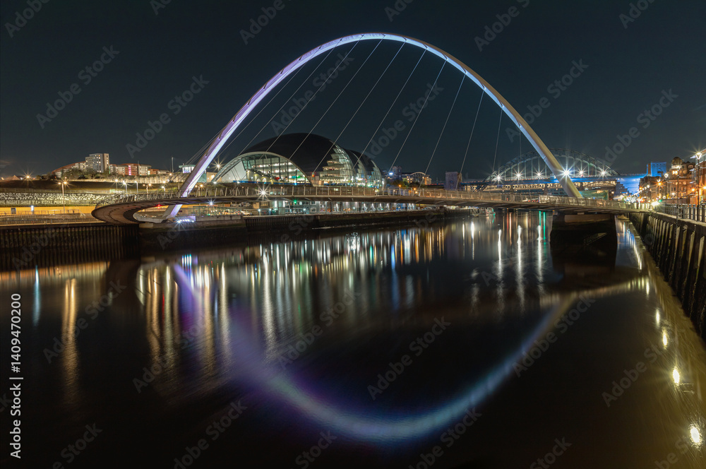 Night view of The Iconic gateshead millennium bridge spanning the River Tyne with Sage Gateshead with Tyne Bridge in the background. The pedestrian bridge with reflection in river, Space for text.