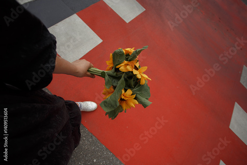 Young woman holds a bouquet of sunflowers in her hand on the  bright red pedestrian crossing background.