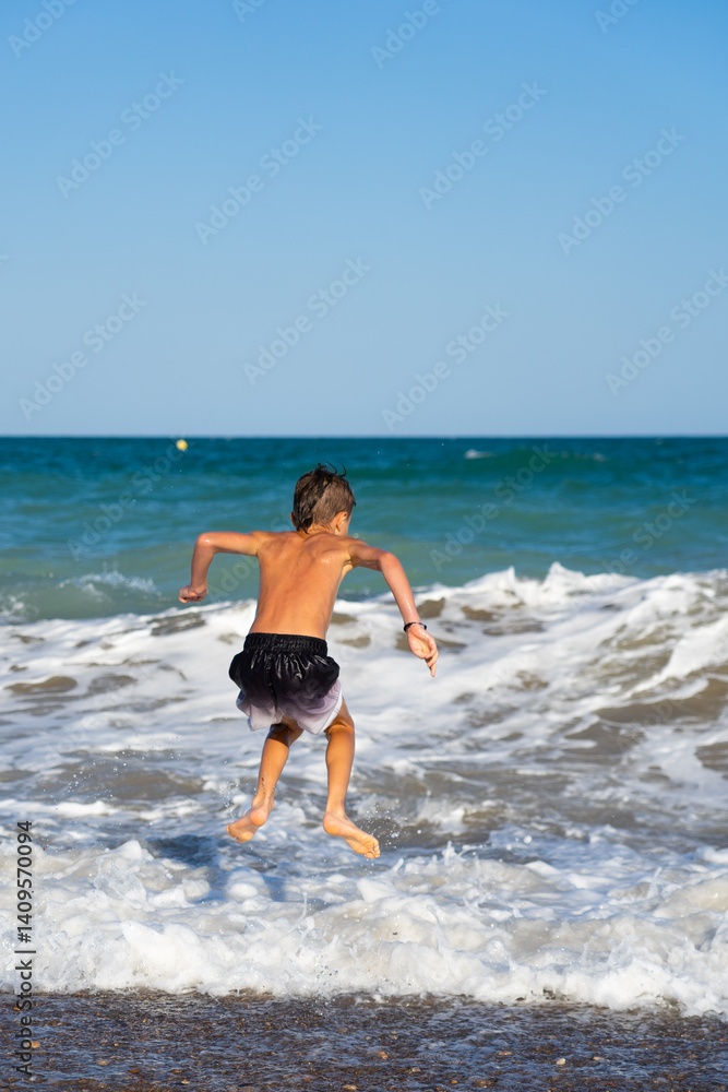 Fototapeta premium Boy jumping over waves on beach summer vacation fun