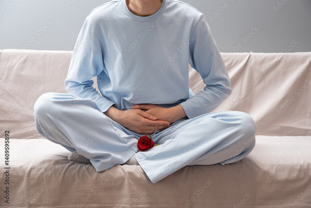 Obraz premium A girl in blue pajamas holds her stomach. There is a red rose next to her as a symbol of menstruation. Depression