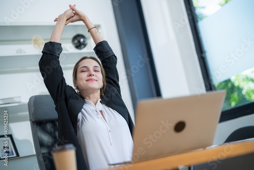 Woman stretches at her desk in a bright office space during a work break with a laptop open in front of her