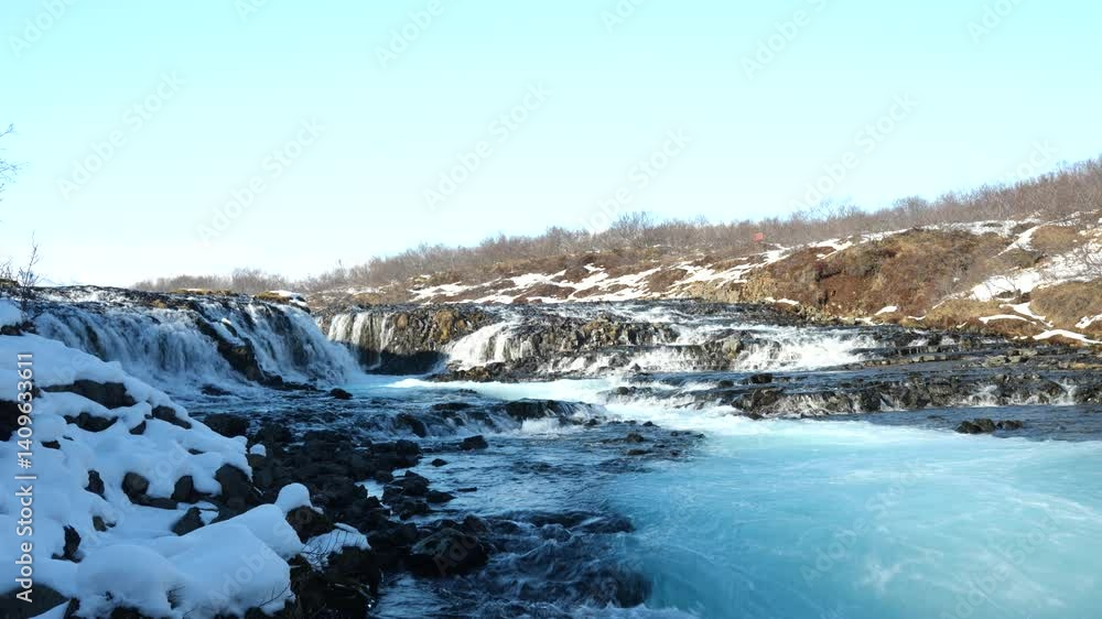 Stunning view of Brúarfoss waterfall in Iceland, known for its icy blue glacier water flowing over lava rocks, surrounded by snow-covered terrain. Stunning view of Brúarfoss waterfall in Iceland, known for its icy blue glacier water flowing over lava rocks, surrounded by snow-covered terrain.