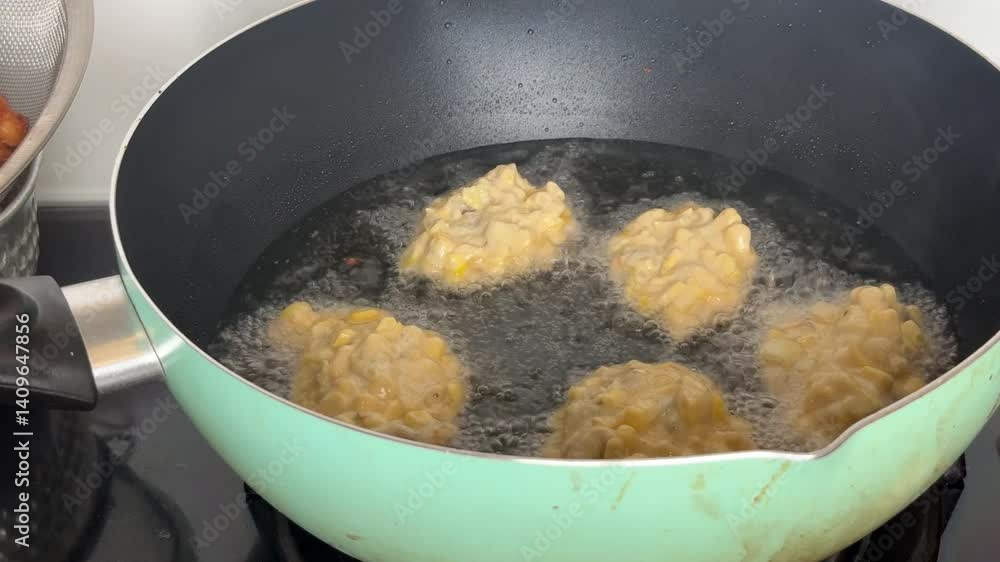 Crispy Indonesian fried corn fritters, bakwan jagung being deep fried in a pan with hot oil, and freshly cooked ones draining in a metal strainer. A popular Ramadan snack for breaking the fast. Crispy Indonesian fried corn fritters, bakwan jagung being deep fried in a pan with hot oil, and freshly cooked ones draining in a metal strainer. A popular Ramadan snack for breaking the fast.