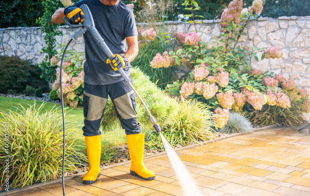 Man Using Pressure Washer to Clean Patio in Garden