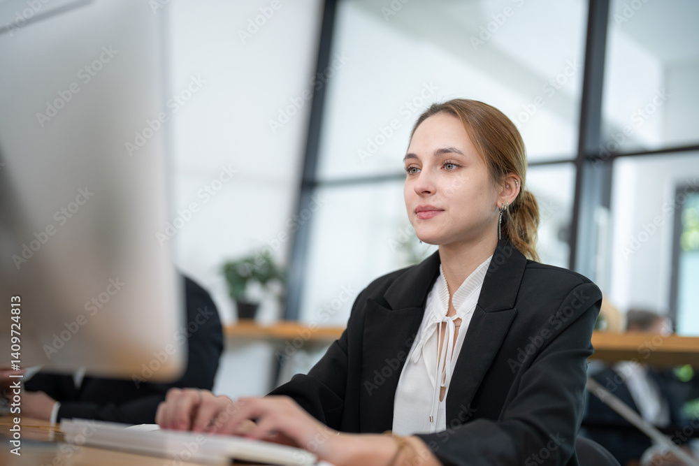 Professional woman working on computer in modern office with large windows during daylight hours Professional woman working on computer in modern office with large windows during daylight hours