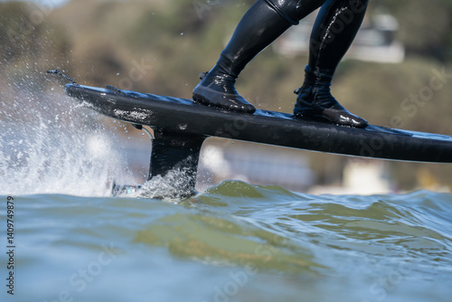 Photography Close up of an man's legs standing on riding an electric powered hydrofoil trench board surfboard, in the the sea on a sunny day, efoil, foil drive, hybrid foil assist