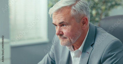 Wallpaper Mural A mature man with gray hair and stubble wearing a navy shirt at his desk in a business room, stares at his laptop screen, taps his fingers on the keyboard, sends emails to co-workers, signs reports Torontodigital.ca