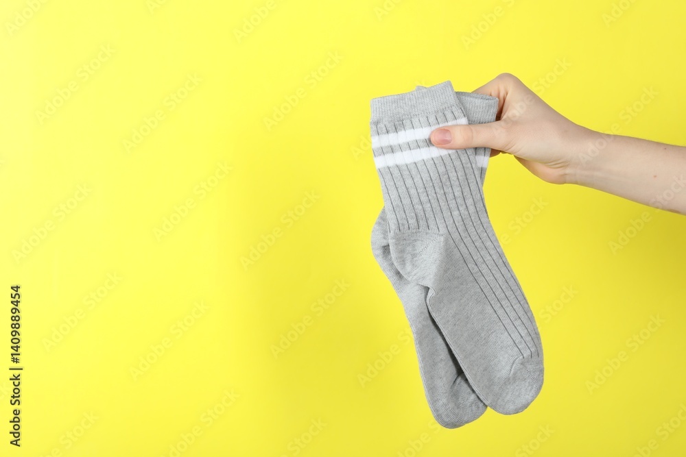 Woman with pair of socks on yellow background, closeup. Space for text