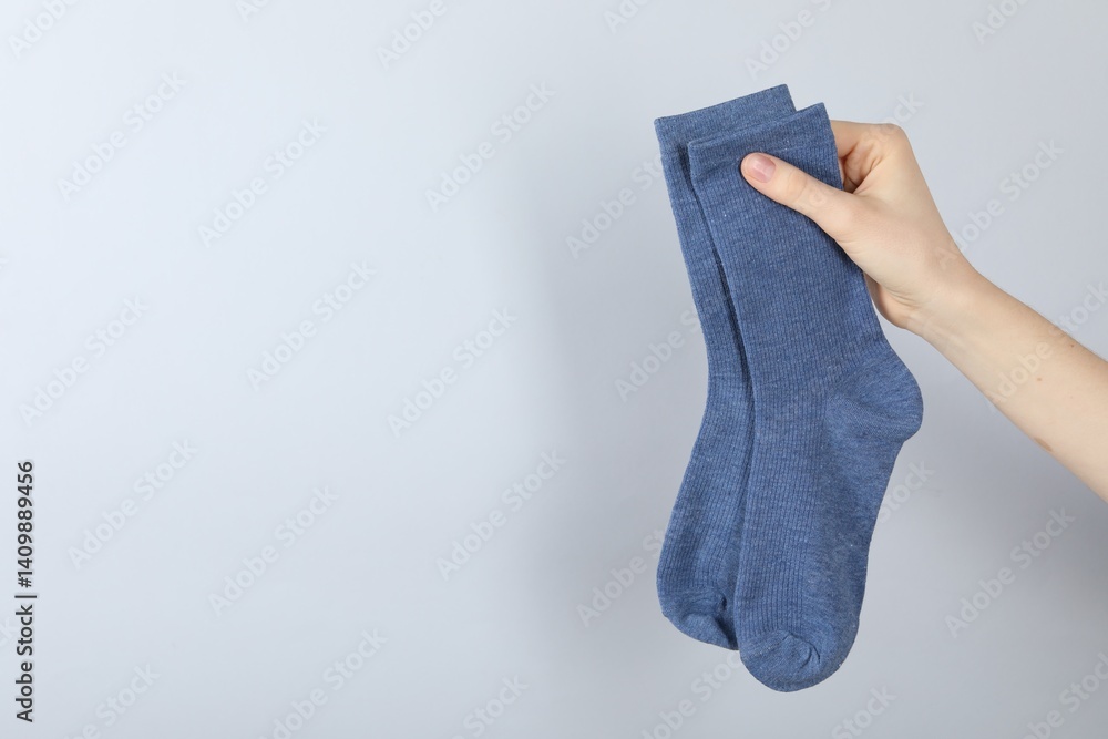 Woman with pair of socks on light grey background, closeup. Space for text