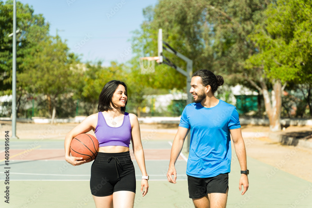Obraz premium Cheerful Latin couple walking and talking on outdoor basketball court